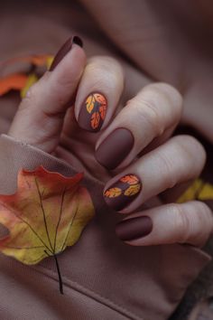 Capture the essence of fall with these chic brown nails, adorned with vibrant orange and yellow leaf designs. Perfect for the fashion-forward, this trendy fall nail design adds a seasonal touch to your look. Whether you're cozying up for the season or attending an autumn event, these stylish nails are the perfect accessory to elevate your fall fashion game! Fall Leaf Design Nails, November Themed Nails, Oval Nails Halloween, Leaf Nails Fall, Brown And Orange Nails Fall, Yellow Autumn Nails, Fall Leaves Nail Designs, Orange And Red Nails, Fall Nails Leaves