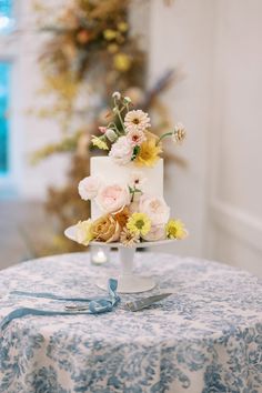 a white and blue wedding cake with flowers on it sitting on top of a table