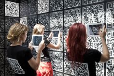 two women are looking at qr - code on a wall with their cell phones