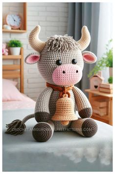 a crocheted cow sitting on top of a bed next to a clock and window