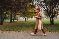 a woman is walking down the street while looking at her cell phone and wearing a red hat