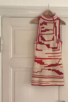 a red and white knitted dress hanging on a door hanger in front of a white door