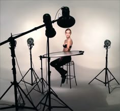 a woman is sitting at a table in front of several light stands and lighting equipment