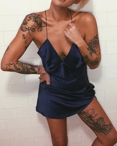 a woman with tattoos on her arms and legs standing in front of a white tiled wall