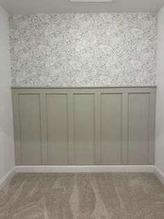 an empty room with white paneling and wallpaper on the walls, in front of a carpeted floor