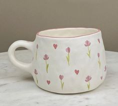 a white cup with pink flowers and hearts painted on the inside is sitting on a marble table