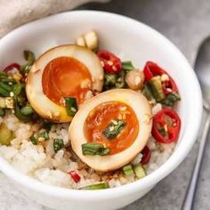 two eggs are on top of rice in a white bowl with silverware next to it