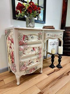 an antique dresser with roses painted on it and candles in front of the drawers, next to a candle holder