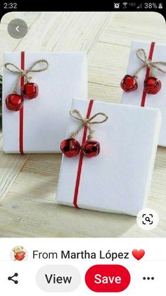 two white gift boxes wrapped in red ribbon and with bells tied around them, sitting on top of a wooden table