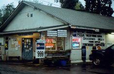 an old gas station with signs on the side of it and a car parked in front