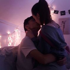 a man and woman kissing in bed with lights on the wall behind them at night