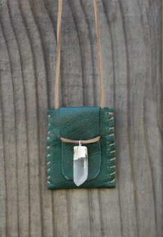 a green leather purse hanging on the side of a wooden wall with a white tag attached to it