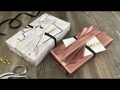 two wrapped presents sitting on top of a wooden floor next to scissors and paper flowers