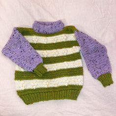 a green and white sweater laying on top of a bed next to a stuffed animal