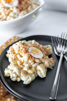 a black plate topped with macaroni and cheese next to a bowl of eggs