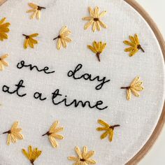 the embroidery is written on a white cloth with gold leaves and words that read, one day at a time