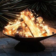 a bowl filled with lights and logs on top of a stone floor next to plants