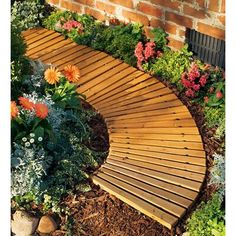 a curved wooden walkway surrounded by flowers and greenery in the foreground is brick wall