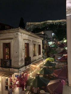 an old building is lit up at night with umbrellas and tables in the foreground