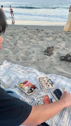 a man sitting on top of a beach next to the ocean eating sushi and chopsticks