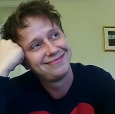 a young man smiles as he poses for the camera with his hand on his head