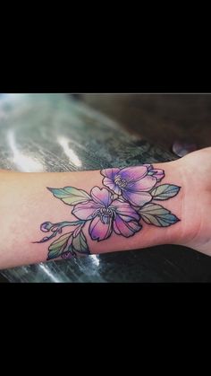 a woman's arm with flowers on it and leaves around the wrist tattoo design