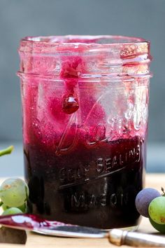 a jar filled with liquid sitting on top of a table next to grapes and a knife