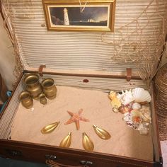 an open suitcase with seashells and starfish on the sand in front of a painting