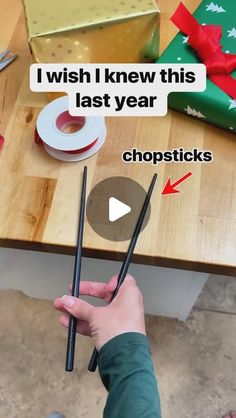 someone is holding two chopsticks in their hand and they have wrapped presents on the table