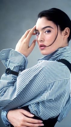 a woman wearing a striped shirt and black suspenders poses for a photo with her hand on her head