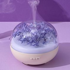 a humidifier with purple flowers in it sitting on a table next to a wall