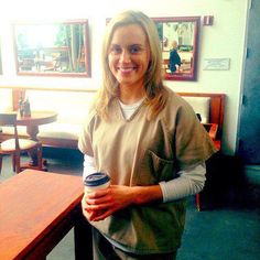 a woman holding a coffee cup in her right hand and smiling at the camera while standing next to a table