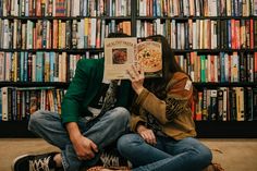 a woman sitting on the floor reading a book in front of a library full of books