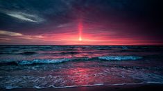 the sun is setting over the ocean with waves crashing in front of it and red sky