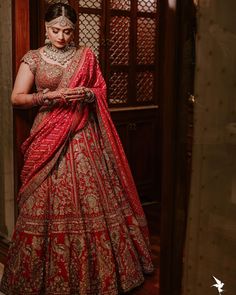 a woman in a red and gold bridal gown standing by a door with her hands on her hips