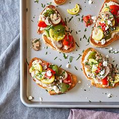 several slices of bread topped with veggies and cheese on a baking sheet next to a purple towel