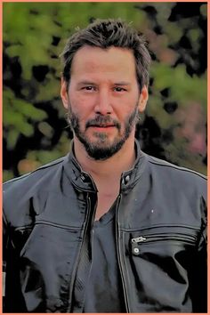 a man wearing a black leather jacket standing in front of trees