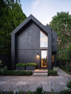 a black house with steps leading to the front door and side entrance, surrounded by greenery