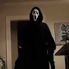 a person in a black hoodie with a white mask on standing in a dark room