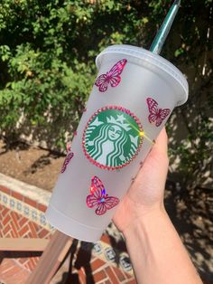 a hand holding a starbucks cup with butterfly decals on the side and a straw in it