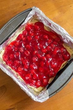 an uncooked cake with cherries on top in tin foil sitting on a wooden table