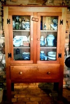 a wooden china cabinet with glass doors and shelves on the top, in front of a brick wall