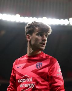 a young man in a red shirt standing on a soccer field with his head turned to the side