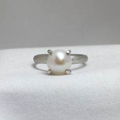 This edgy ring features a beautiful fresh water pearl, which I set in a handmade sterling silver square prongs.  A modern, contemporary look is a fresh take on a classic.  A lightly brushed finish sets off the ring, or you may order it in an oxidized (darkened) finish if you prefer. Size:   5.5 US Pearl:    ~ 7.5 mm Band:   ~ 2.5 mm Silver Minimalist Pearl Ring For Everyday Wear, Minimalist White Gold Pearl Drop Ring, Minimalist Pearl Drop Ring, Elegant White Gold Jewelry With Brushed Finish, Modern Sterling Silver Pearl Ring For Gift, Modern Sterling Silver Pearl Ring As Gift, Minimalist White Gold Ring With Pearl Drop, Modern White Gold Sterling Silver Pearl Ring, Minimalist White Gold Pearl Ring