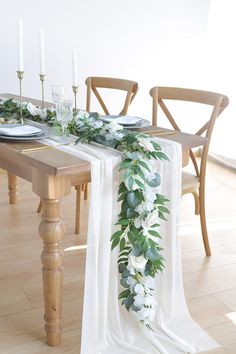 the table is set with white flowers and greenery on it, along with candles