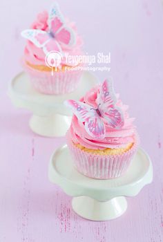 two cupcakes with pink frosting and butterflies on them are sitting on plates