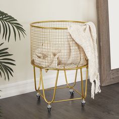 a white blanket is sitting on top of a wire basket next to a potted plant