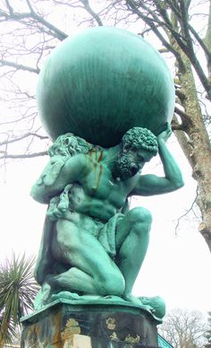 black and white photograph of a statue holding a large object on top of it's head