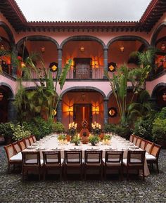 an outdoor dining area with tables, chairs and potted plants in front of a pink building