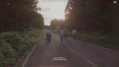 several people walking down the road with trees in the background